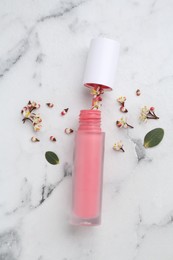 Photo of Pink lip gloss, flowers and green leaves on white marble table, flat lay