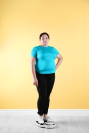 Photo of Overweight woman in sportswear using scales near color wall