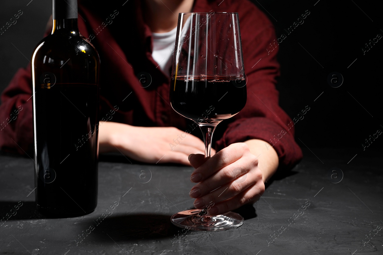 Photo of Alcohol addiction. Woman with red wine at dark textured table, selective focus