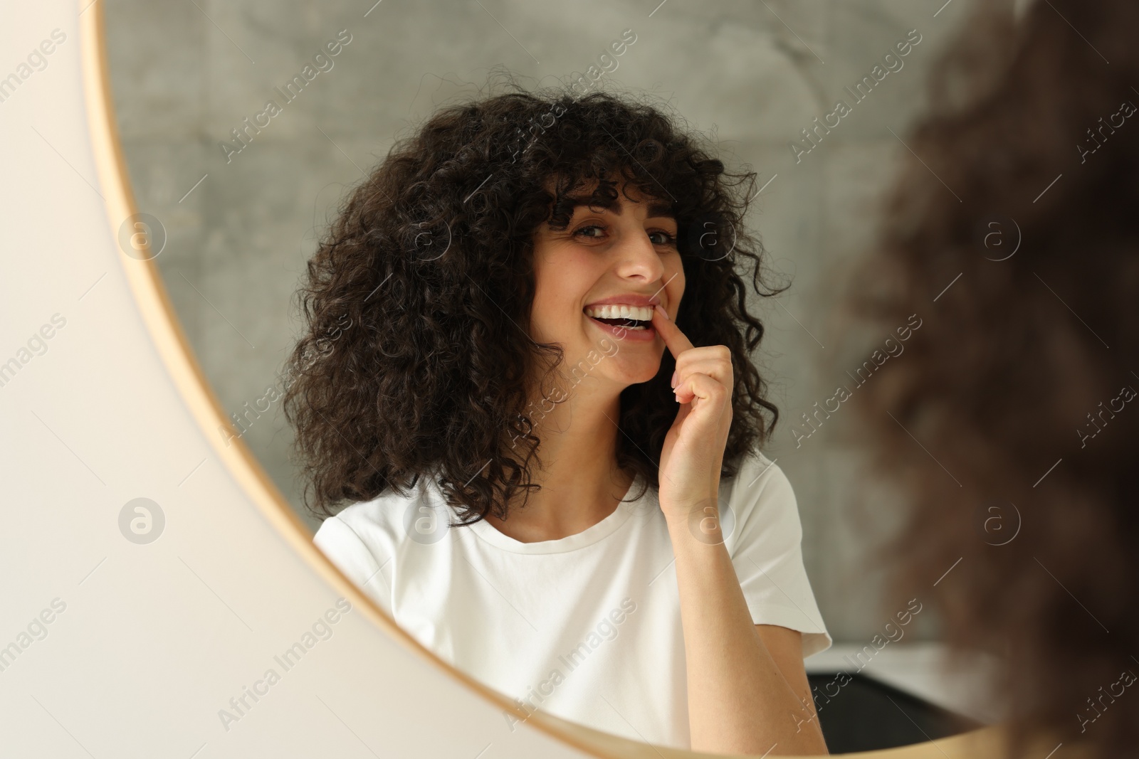 Photo of Young woman applying whitening strip on her teeth indoors