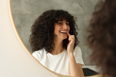 Photo of Young woman applying whitening strip on her teeth indoors