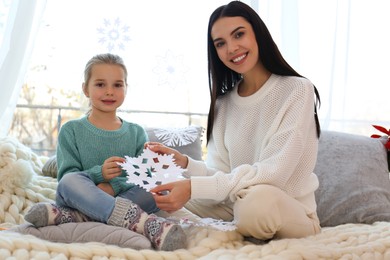 Photo of Mother and daughter with paper snowflake near window at home