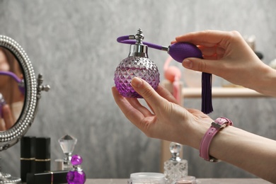 Photo of Woman holding luxurious perfume in crystal vintage bottle over dressing table, closeup