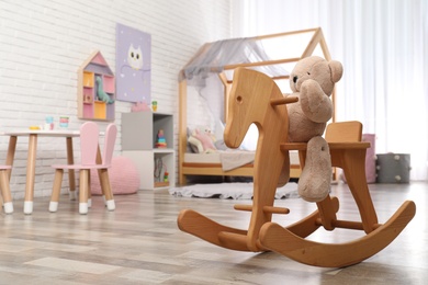 Photo of Teddy bear on wooden rocking horse in child's room, space for text. Interior design