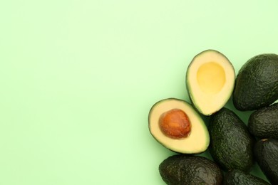 Photo of Tasty whole and cut avocados on light green background, flat lay. Space for text