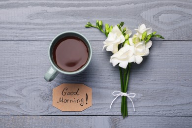 Fresh tea, flowers and Good Morning! message on grey wooden table, flat lay