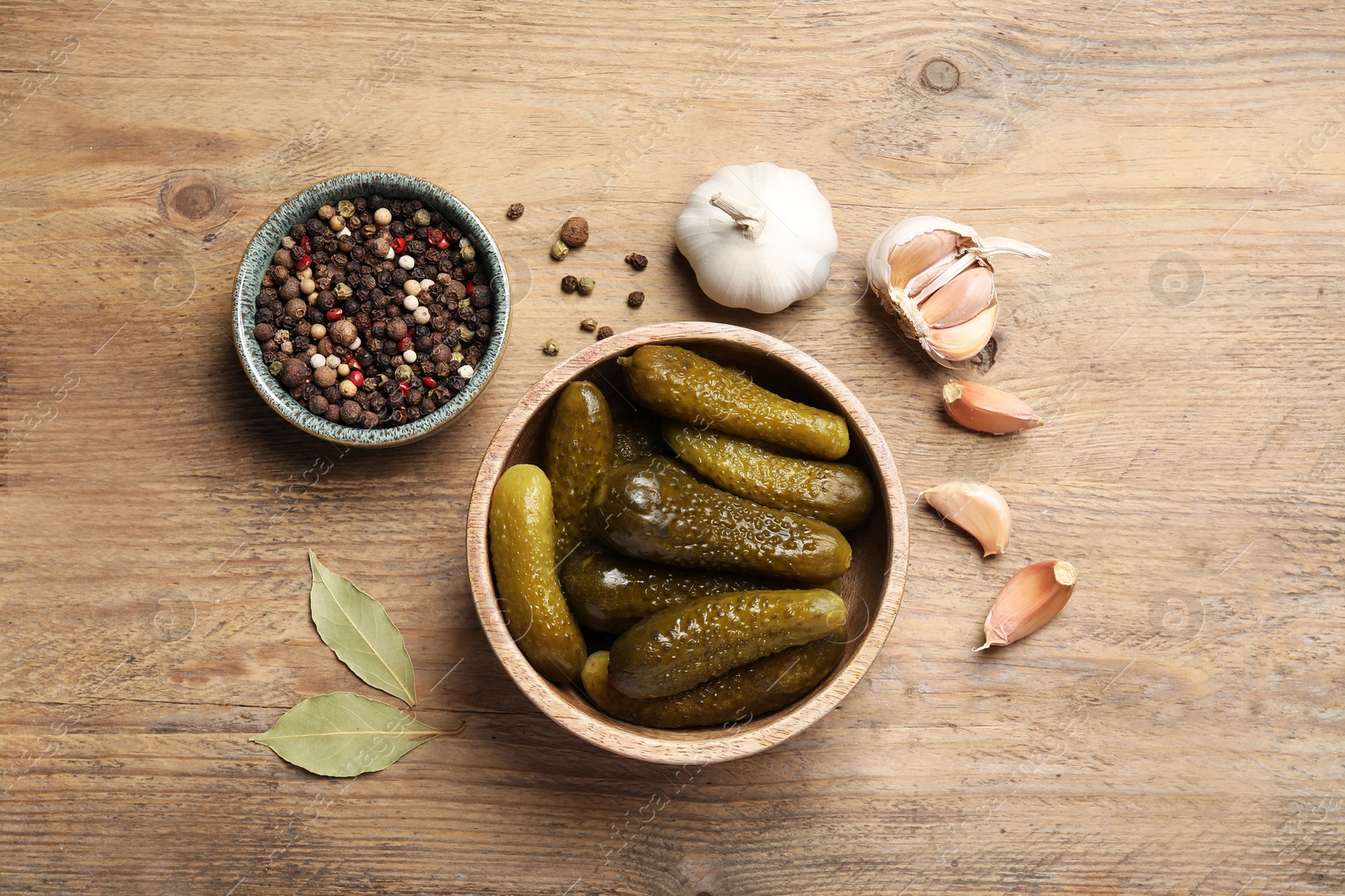 Photo of Tasty pickled cucumbers in bowl and spices on wooden table, flat lay