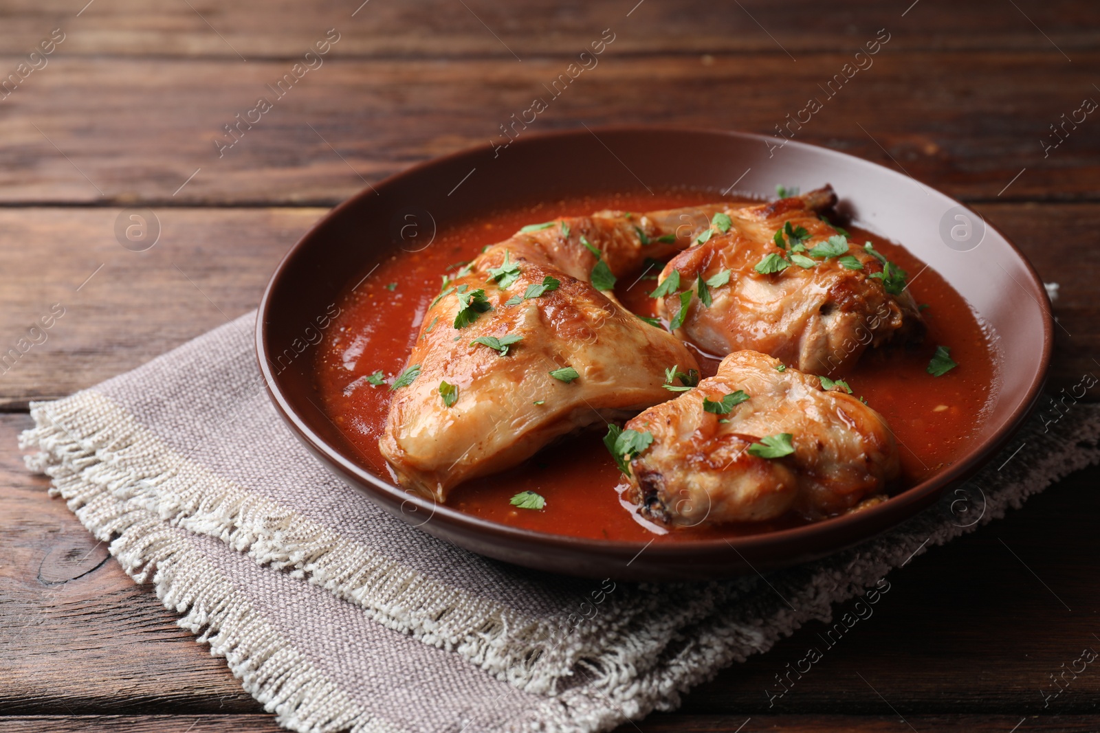 Photo of Tasty cooked rabbit meat with sauce and parsley on wooden table