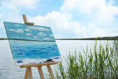 Photo of Wooden easel with unfinished painting near lake