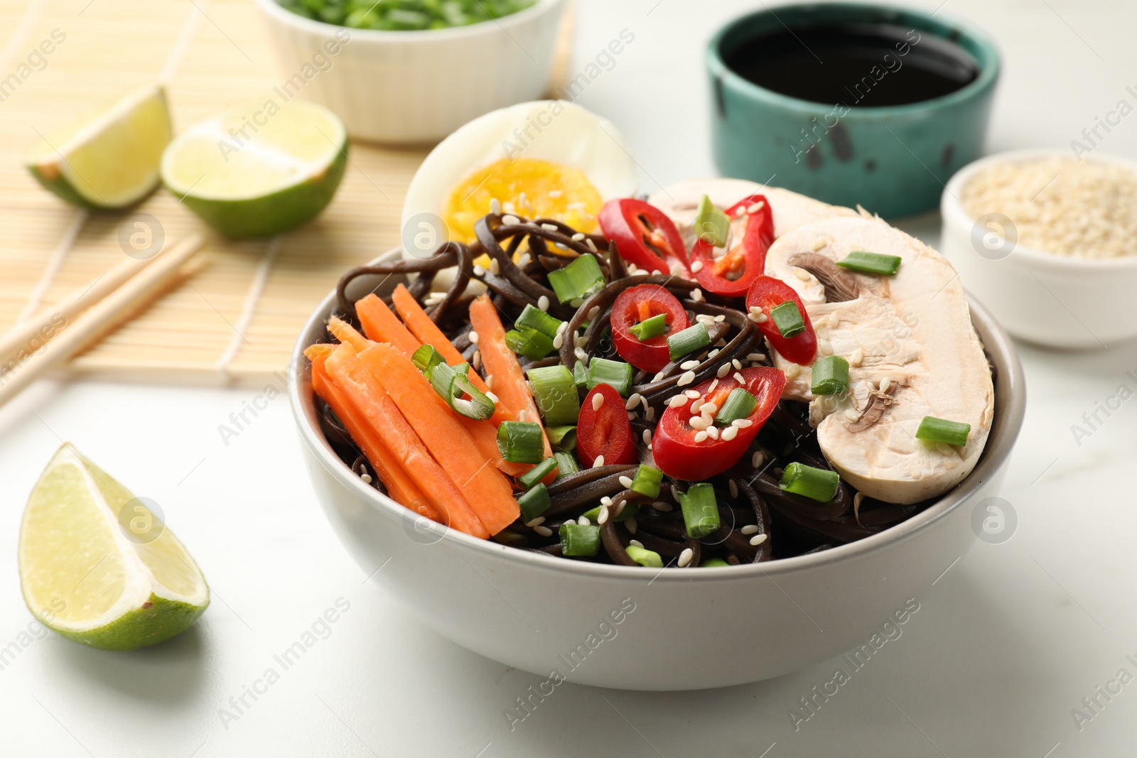 Photo of Tasty buckwheat noodles (soba) with chili pepper, egg, carrot and mushrooms in bowl on white marble table, closeup