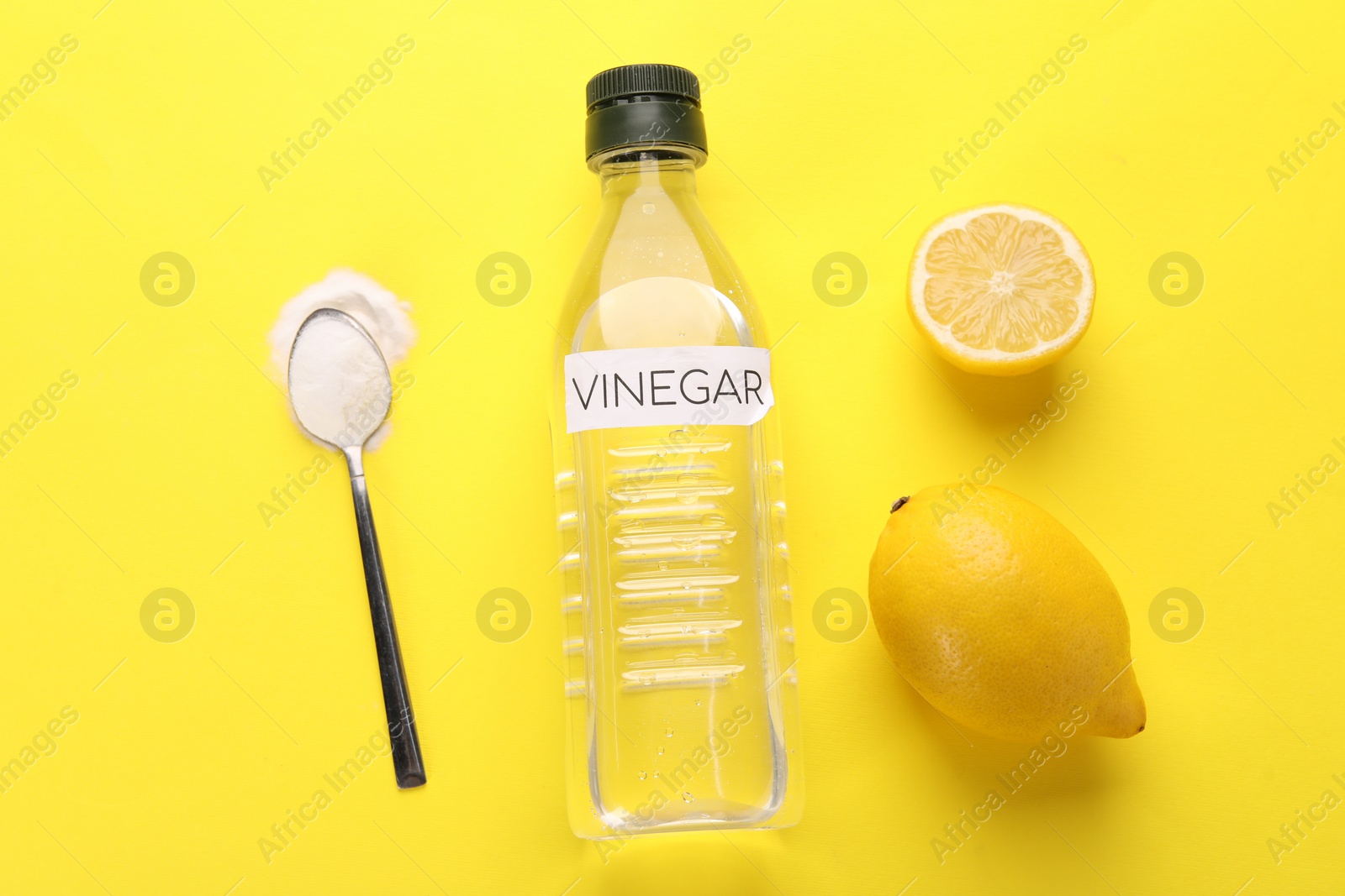 Photo of Eco friendly natural cleaners. Vinegar in bottle, lemons and spoon of soda on yellow background, flat lay