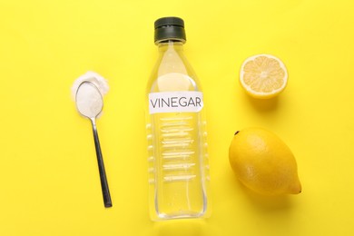 Photo of Eco friendly natural cleaners. Vinegar in bottle, lemons and spoon of soda on yellow background, flat lay