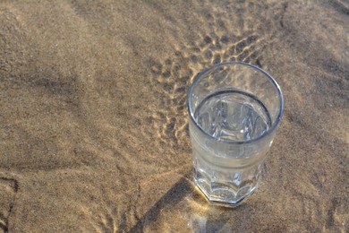 Glass of clean water on wet sand outdoors. Space for text