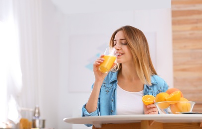 Beautiful young woman drinking orange juice at table indoors, space for text. Healthy diet