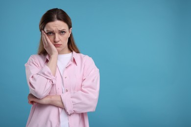 Portrait of sad woman on light blue background, space for text