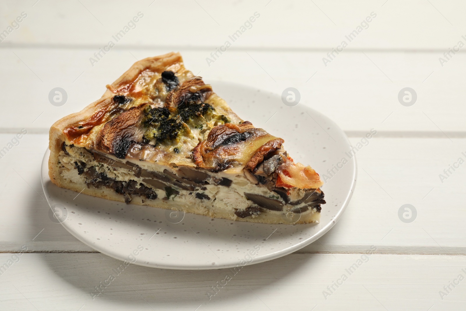 Photo of Piece of delicious quiche with mushrooms on white wooden table