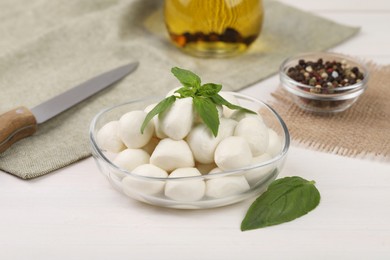 Photo of Tasty mozzarella balls and basil leaves on white wooden table