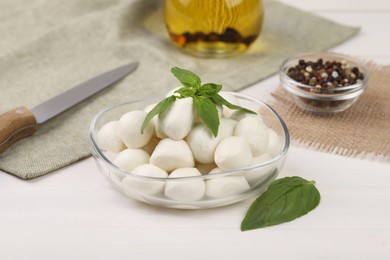 Tasty mozzarella balls and basil leaves on white wooden table