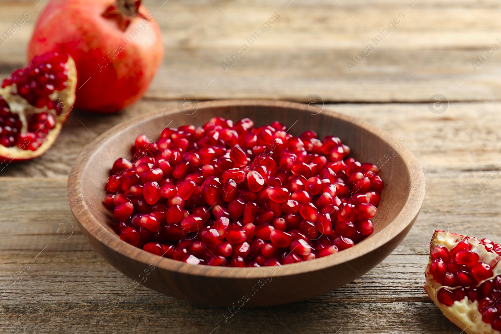 Photo of Ripe juicy pomegranate grains in bowl on wooden table, closeup