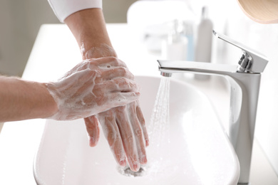 Photo of Man washing hands with soap over sink in bathroom, closeup