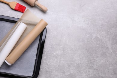 Rolls of parchment paper, baking pan and kitchen tools on light grey table, flat lay. Space for text