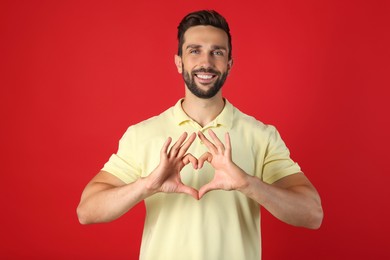 Photo of Happy man making heart with hands on red background