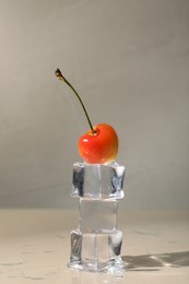 Sweet ripe cherry and stacked ice cubes on beige table