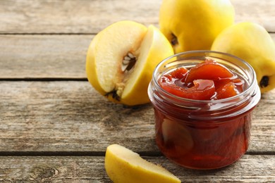 Tasty homemade quince jam in jar and fruits on wooden table, closeup. Space for text