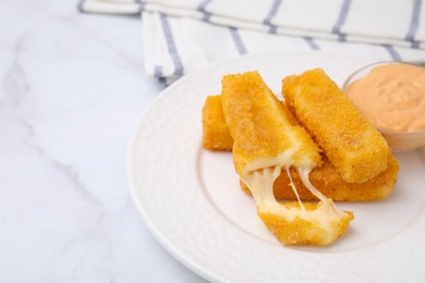 Photo of Plate with tasty fried mozzarella sticks and sauce on white marble table, closeup. Space for text