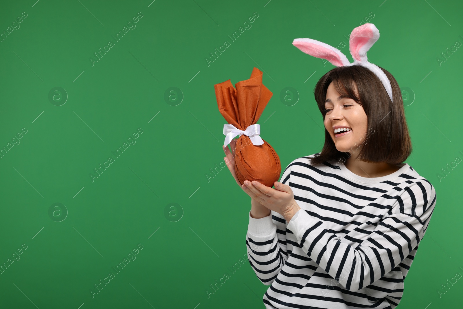 Photo of Easter celebration. Happy woman with bunny ears and wrapped egg on green background, space for text