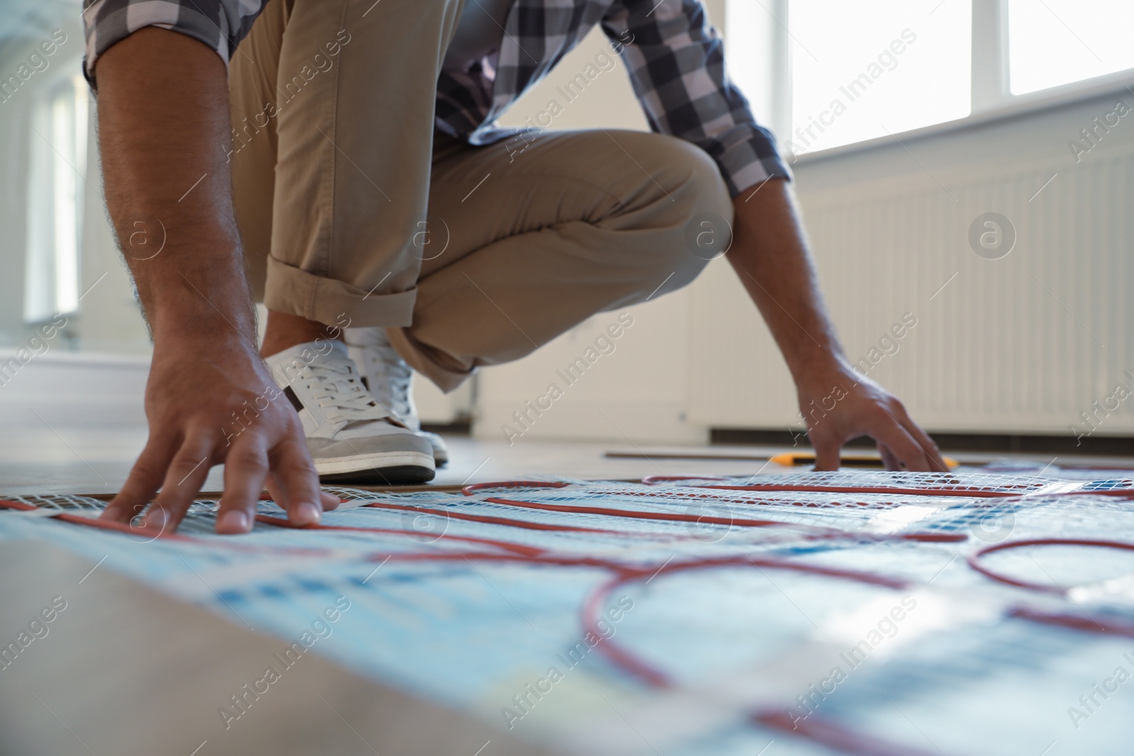 Photo of Professional worker installing electric underfloor heating system indoors, closeup