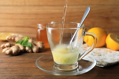 Photo of Pouring hot water into glass cup with grated ginger on wooden table