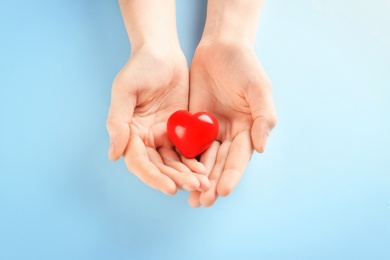 Woman holding small red heart on color background. Heart attack concept