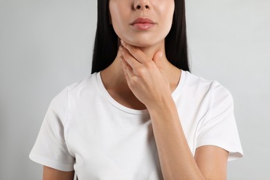 Photo of Young woman doing thyroid self examination on light background, closeup