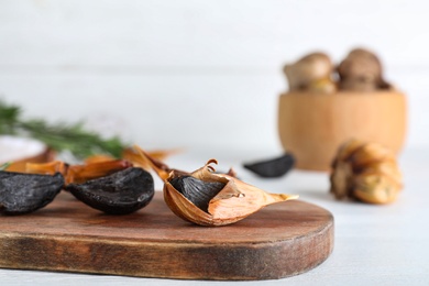 Photo of Wooden board with black garlic on white table. Space for text