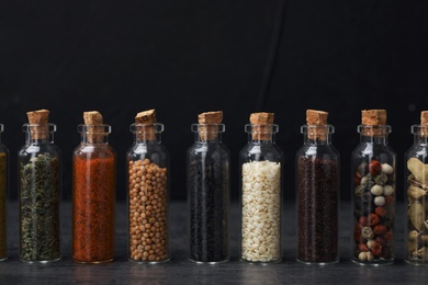 Photo of Glass bottles with different spices on table against black background