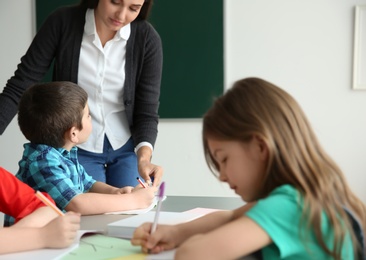 Photo of Female teacher helping boy with his task in classroom at school
