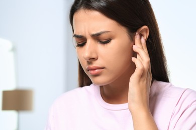 Photo of Young woman suffering from ear pain indoors, closeup