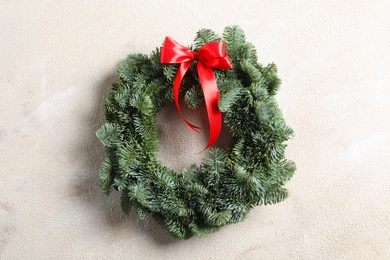 Photo of Christmas wreath made of fir tree branches with red ribbon on light textured background