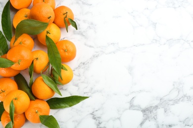Photo of Fresh tangerines with green leaves on white marble table, flat lay. Space for text
