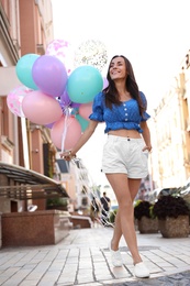 Photo of Beautiful young woman with color balloons on city street