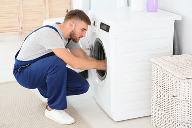 Photo of Young plumber fixing washing machine in bathroom