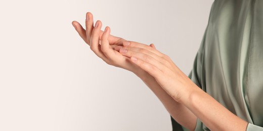 Image of Woman applying cream onto hand on light grey background, closeup. Banner design