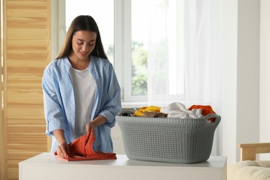 Photo of Young woman folding clean laundry at white table indoors