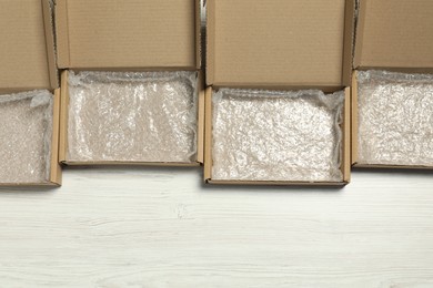Photo of Many open cardboard boxes with bubble wrap on white wooden background, flat lay. Space for text