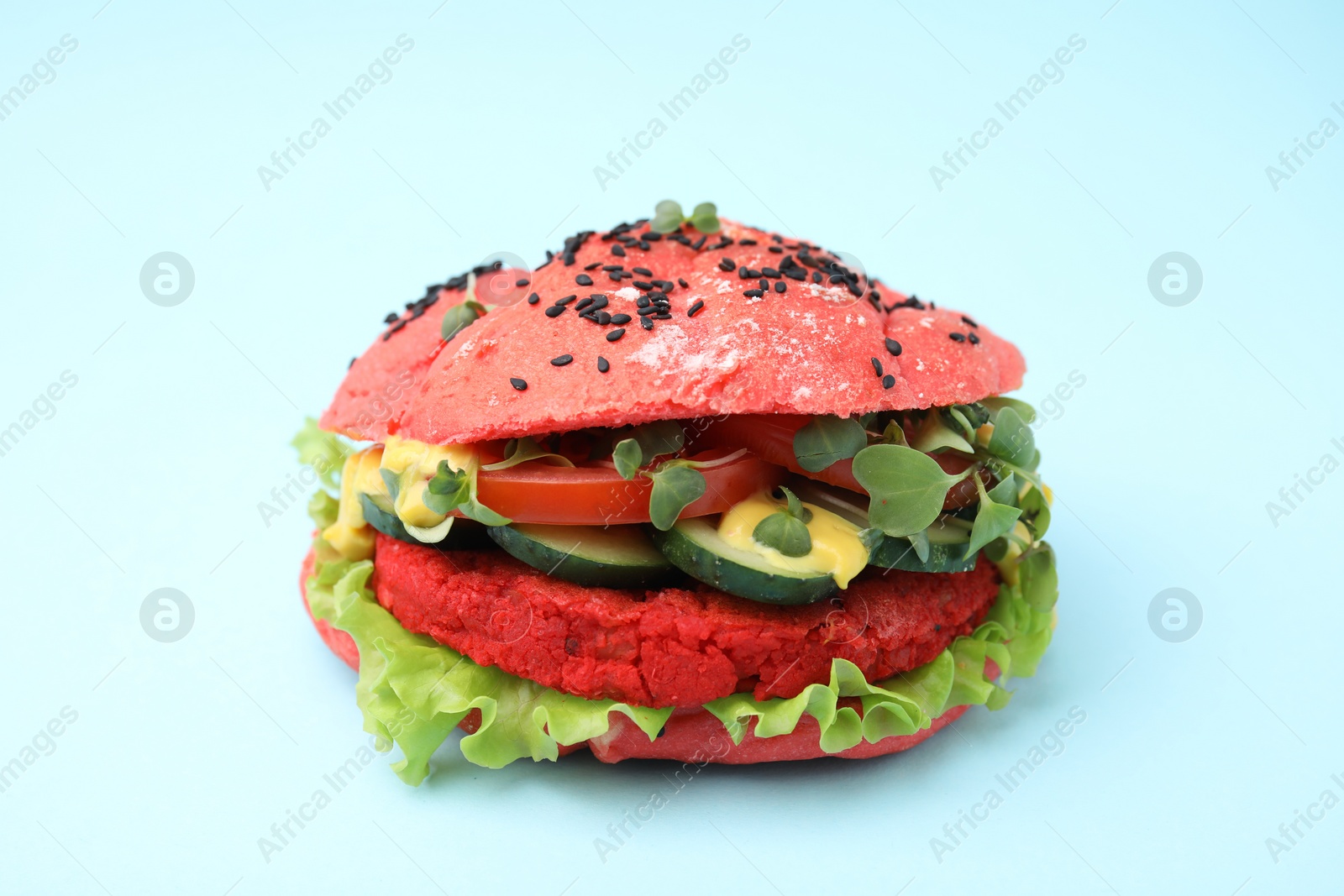 Tasty pink vegan burger with vegetables, patty and microgreens on light blue background, closeup Photo of Tasty pink vegan burger with vegetables, patty and microgreens on light blue background, closeup
