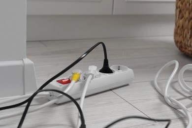 Photo of Extension cord with electrical plugs on white floor indoors, closeup