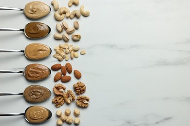 Photo of Tasty nut butters in spoons and raw nuts on white marble table, flat lay. Space for text