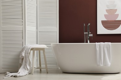 Photo of Modern ceramic bathtub and furniture near burgundy wall in room