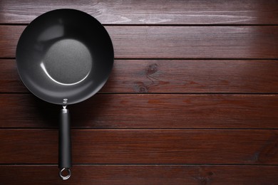 Photo of Empty iron wok on dark wooden table, top view. Space for text